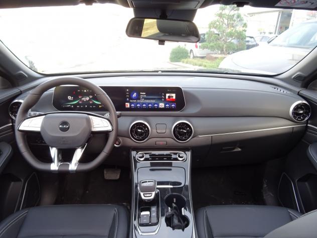 Vista del interior de un automóvil que presenta un tablero de instrumentos moderno con pantalla táctil, volante y selector de marchas. Se ven asientos de cuero negro y varios controles.