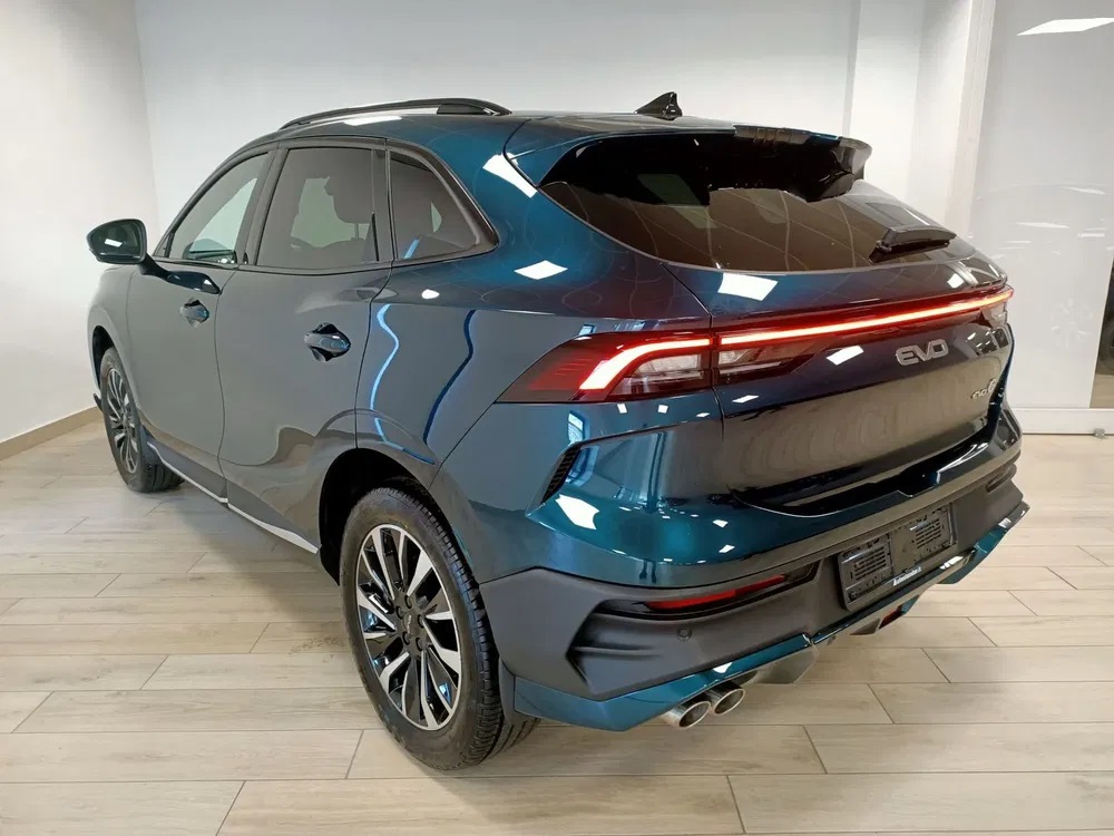 Vista lateral de un SUV azul oscuro en una sala de exposición, con un elegante diseño trasero, tubos de escape dobles y distintivas luces traseras LED.